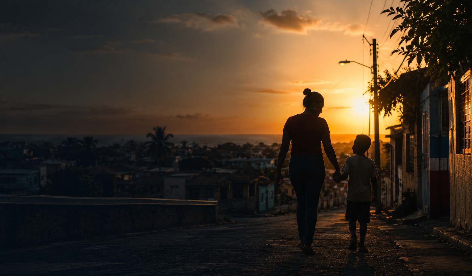 Una madre y su hijo caminan tomados de la mano al atardecer sobre una ciudad dominicana.